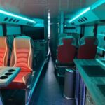 Innenraum eines modernen Luxusbusses mit roten Sitzen, Tischen, Ablagen und blauer Beleuchtung.